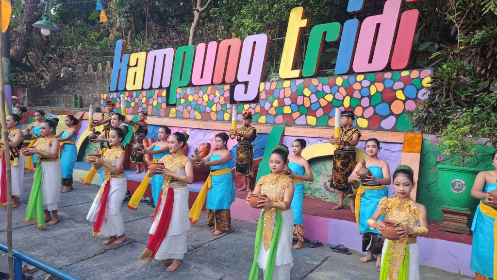 Group of dancers in bright traditional costumes performing with clay pots outdoors in front of a colorful mural wall